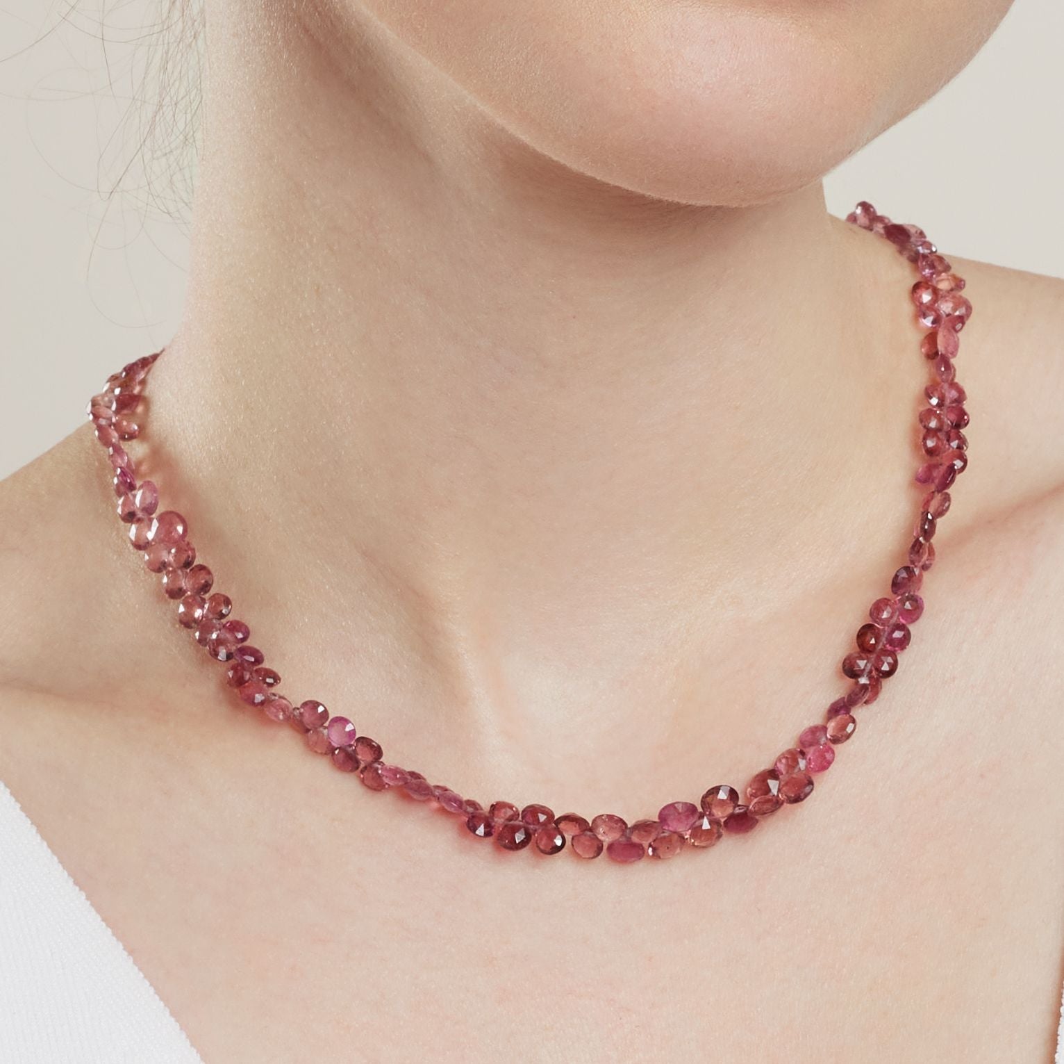 Halssauschnitt einer Frau; sie trägt ein Collier aus doppelt aneinander gereihten kleinen Turmalin-Tropfen in unterschiedlichen Rosé - und Rottönen;