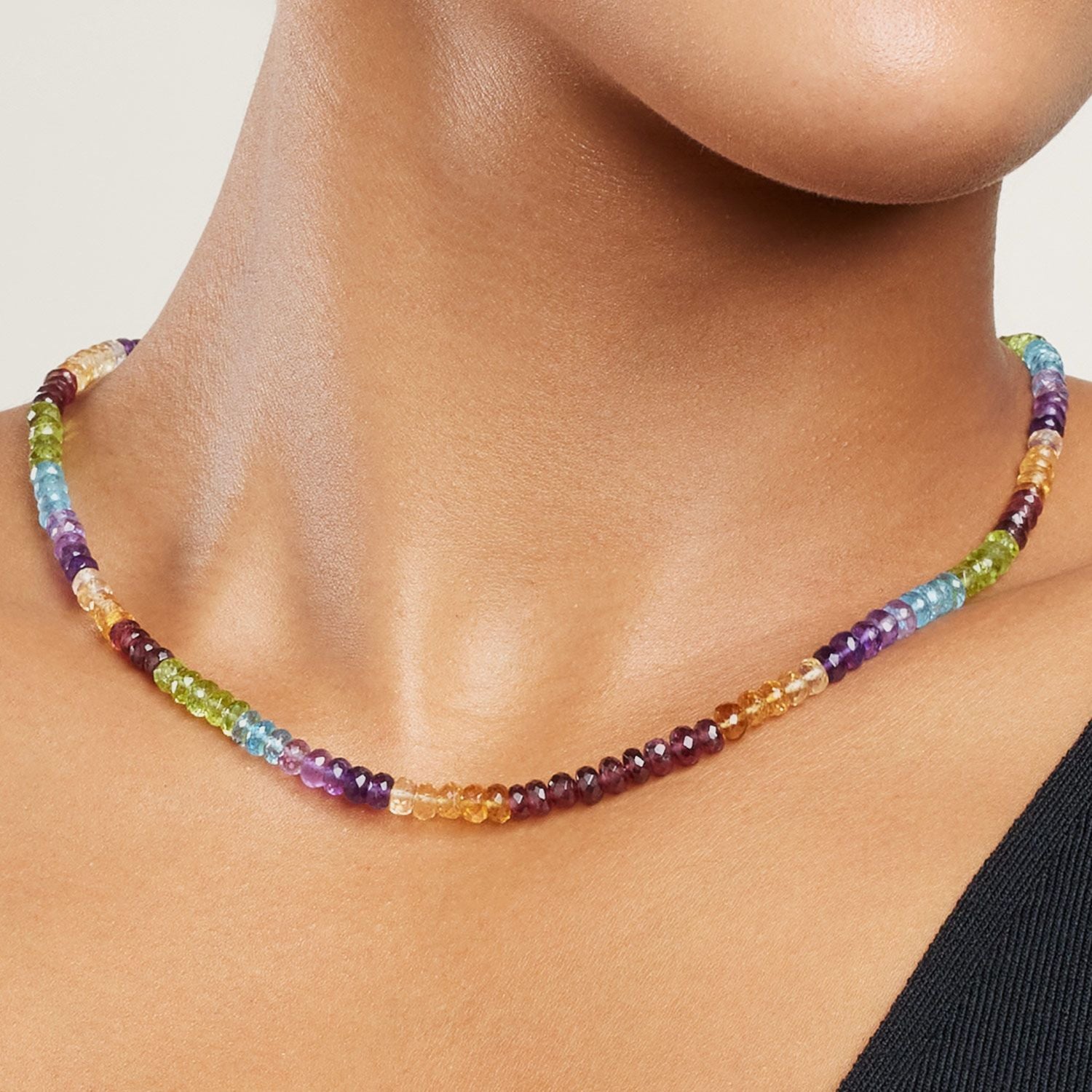 Ausschnitt des Halses einer Frau: sie trägt das Collier mit bunten Steinen aneinander gereiht; jeweils nach vier Steinen wechselt die Farbe;