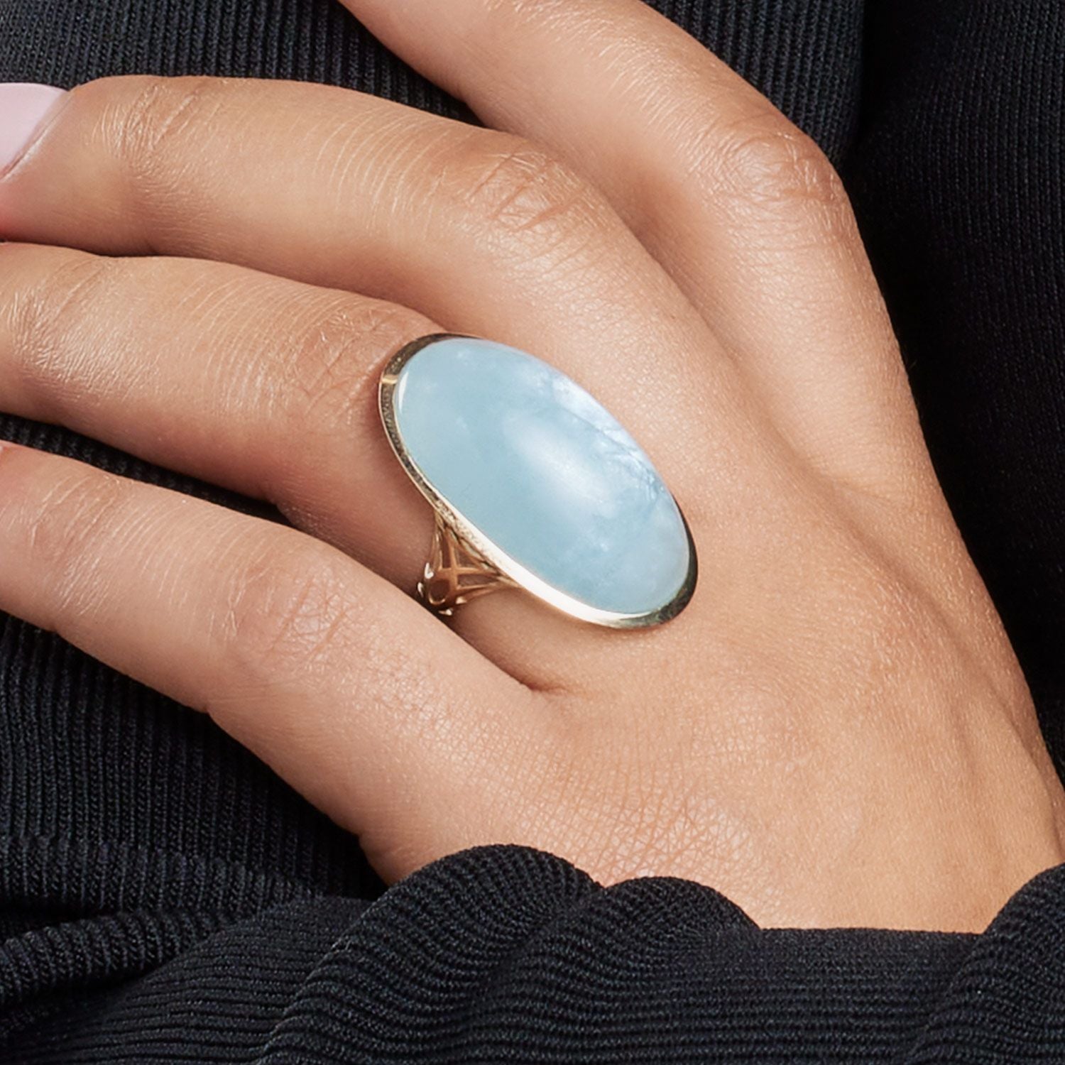 Hand einer Frau; am Ringfinger trägt sie einen Ring in Gelbgold mit einem sehr großen, in Gelbgold gefassten, ovalen, hellblauen Stein;