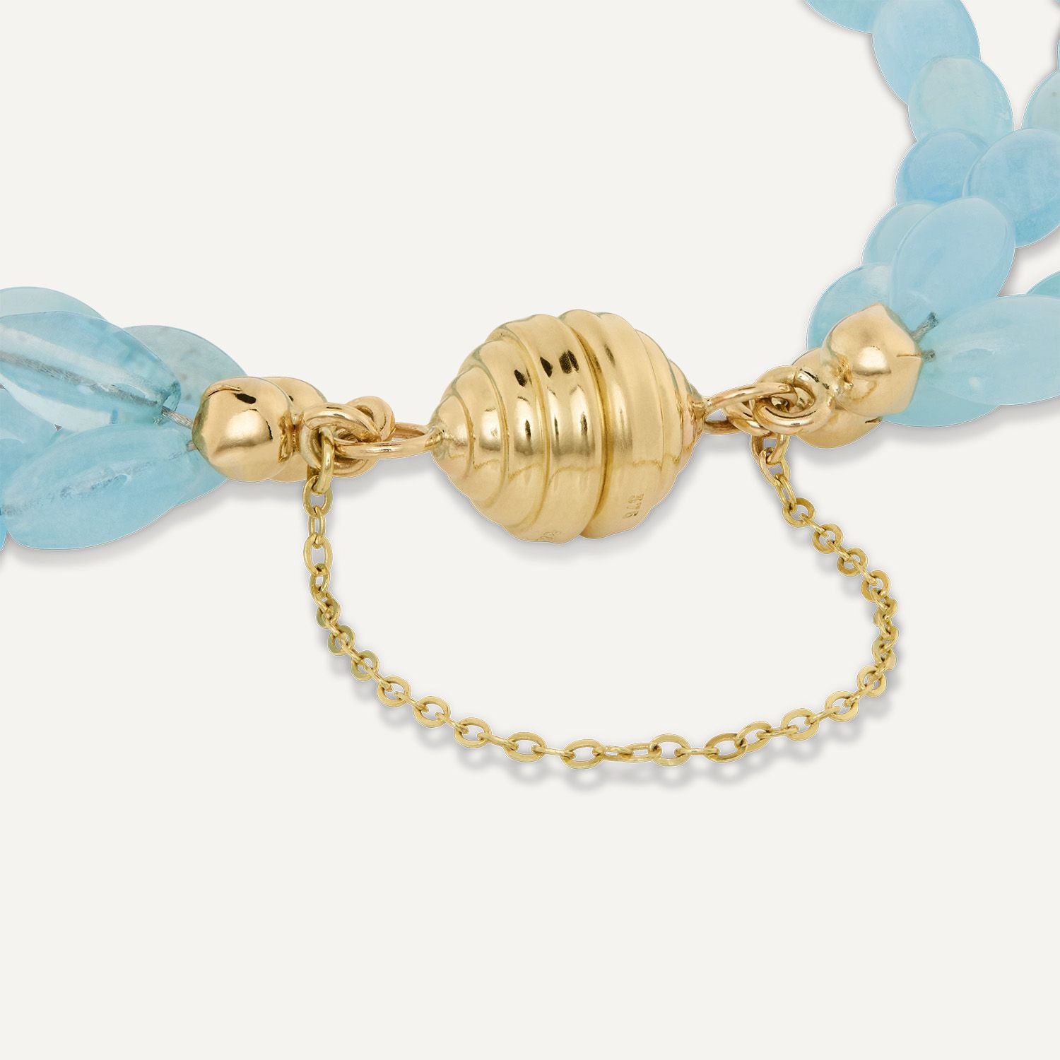 Ausschnitt der goldenen Magnetschließe mit Kette eines vierreihiges Armbands aus direkt aneinander gereihten, hellblauen, ovalen Steinen;