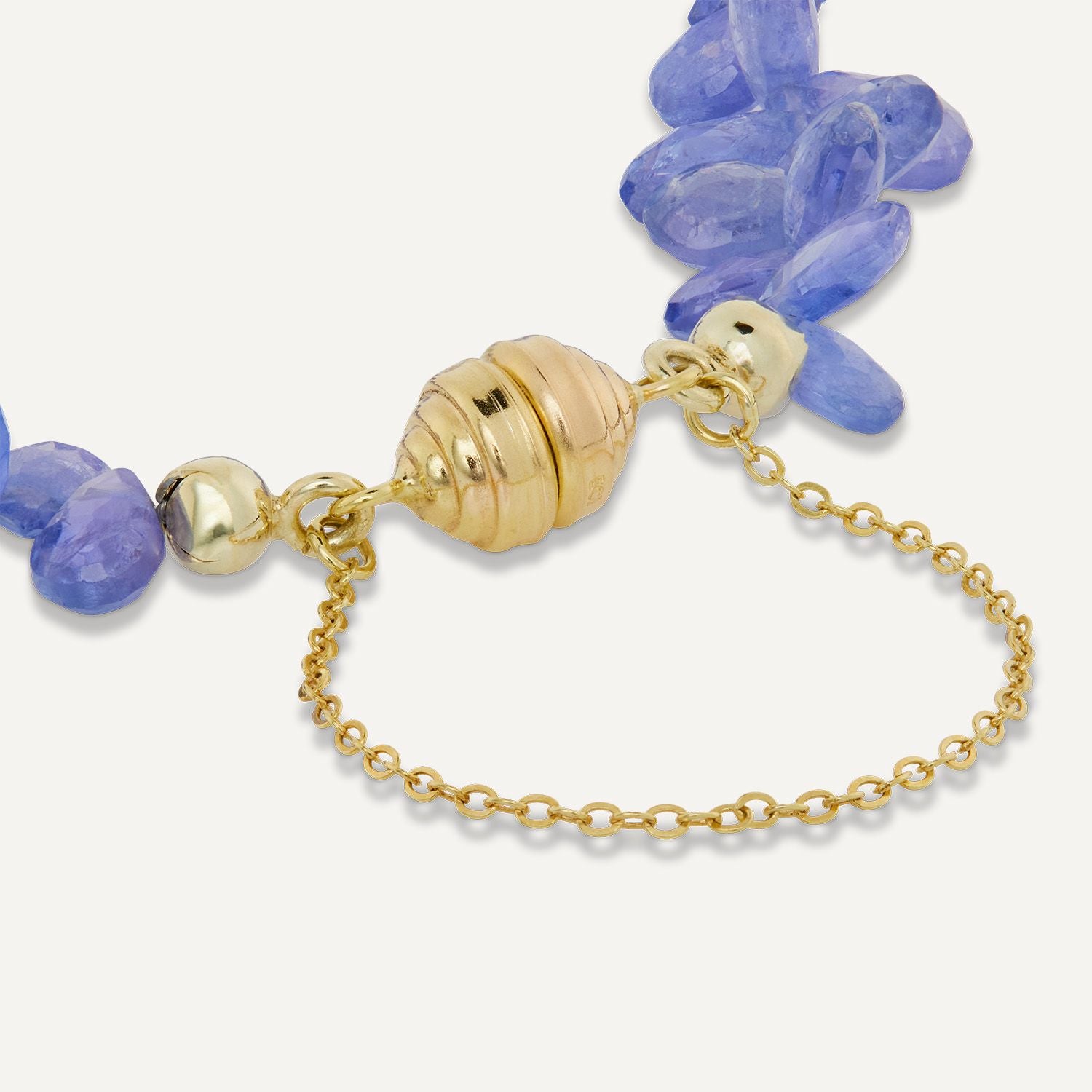 Ausschnitt einer goldenen Magnetschließe mit Kette eines Armbands aus jeweils rechts und links direkt aneinander gereihten, blauen, tropfenförmigen Steinen;
