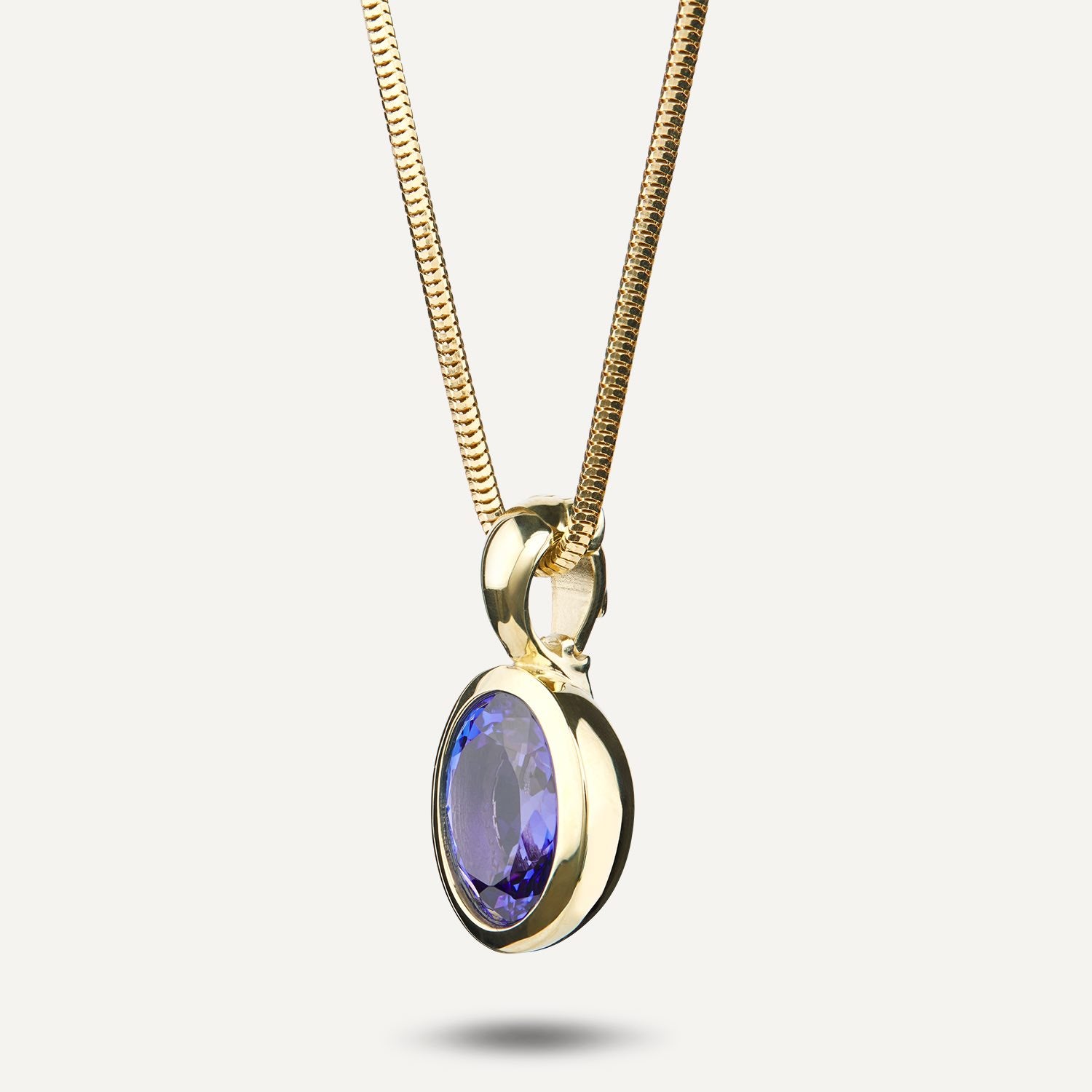 Seitenansicht eines Clip-Anhängers in Gelbgold mit einem in Gelbgold gefassten, runden, blauen Stein an einer Schlangenkette aus Gelbgold;