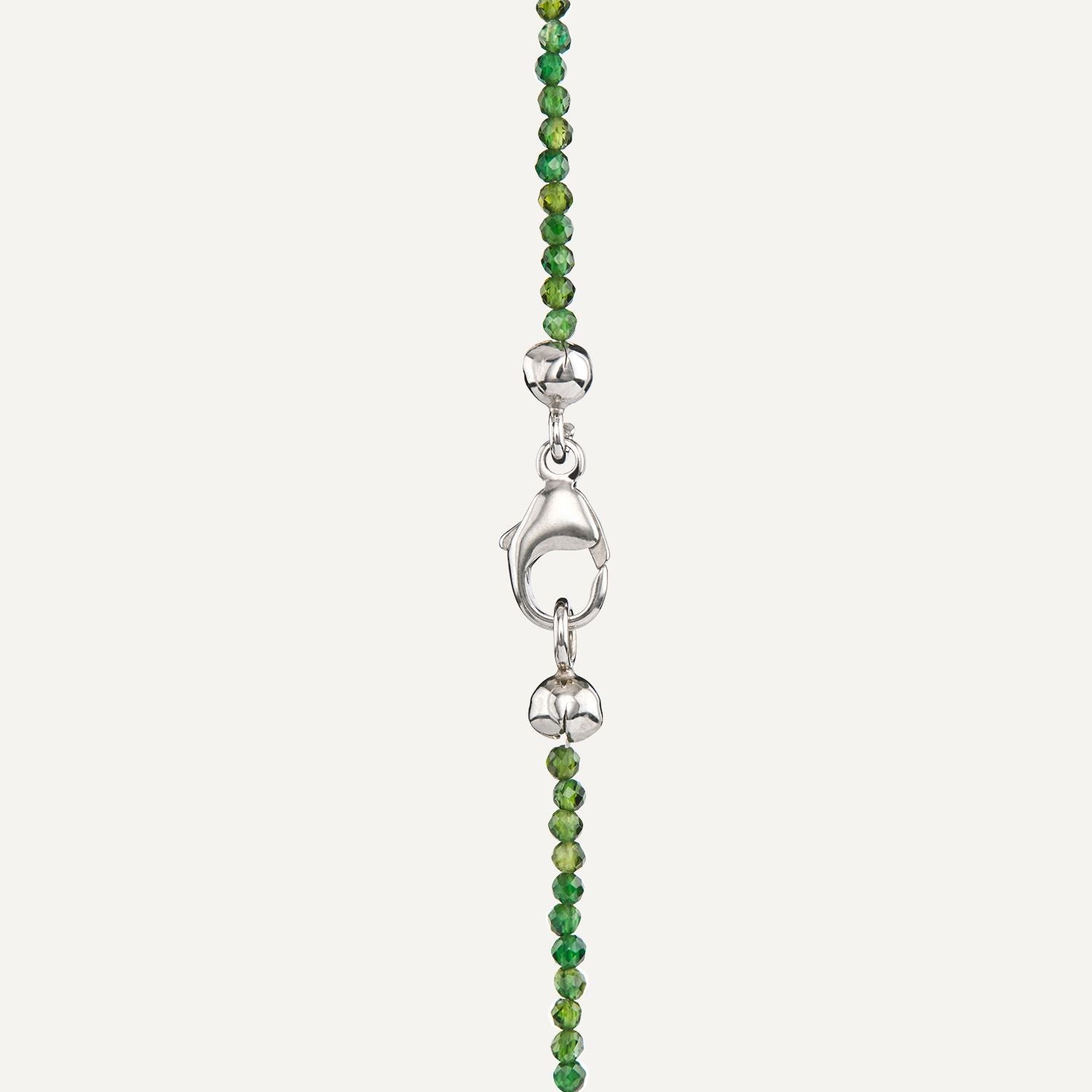 Ausschnitt des silbernen Karabinerverschlusses eines Colliers aus direkt aneinander gereihten, sehr kleinen, runden Steinen in unterschiedlichen Grüntönen;