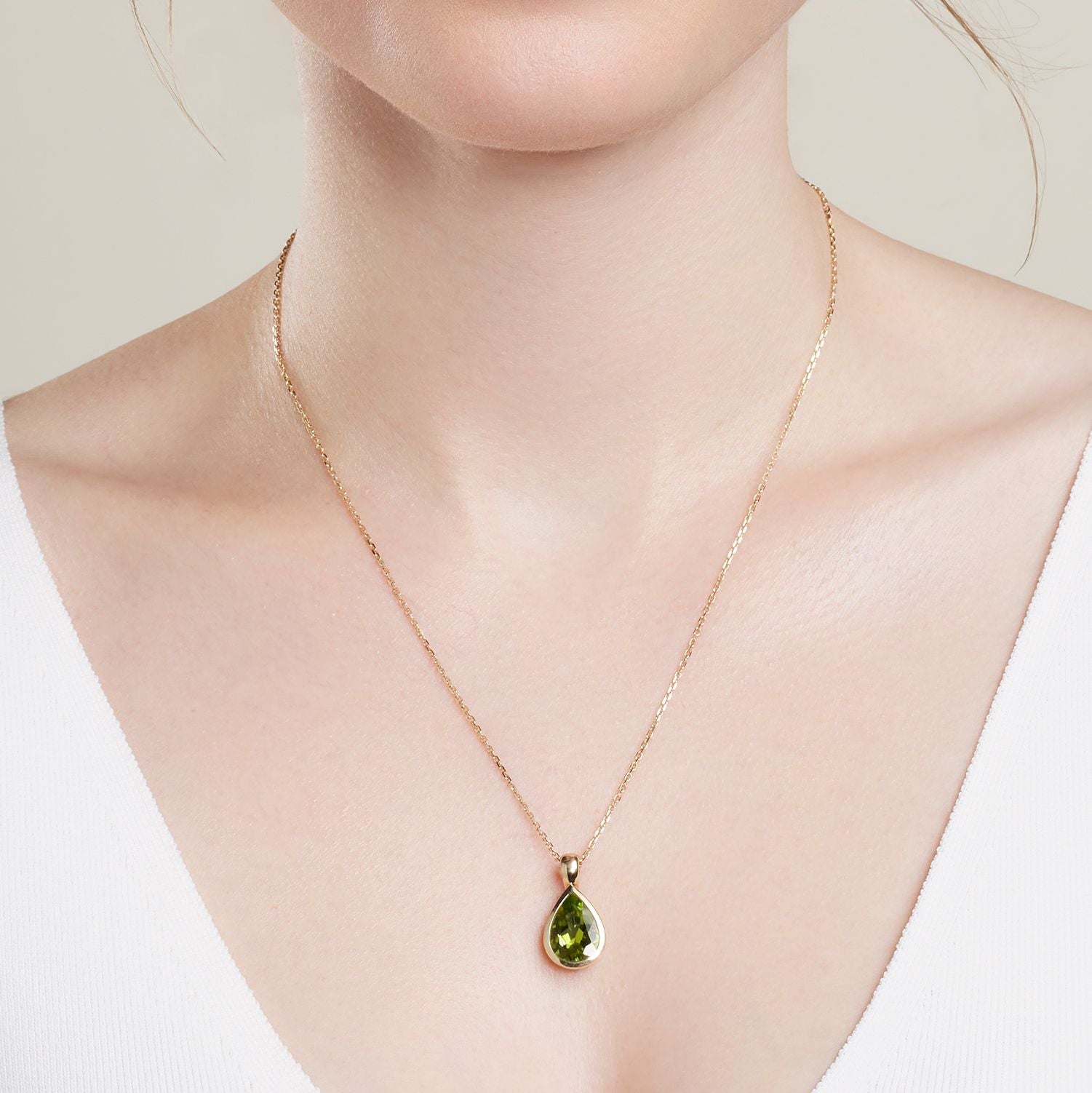 Halsausschnitt einer Frau; sie trägt eine goldene Gliederkette, daran ein Clip-Anhänger aus Gelbgold mit einem in Gelbgold gefassten, grünen Stein in Tropfenform;