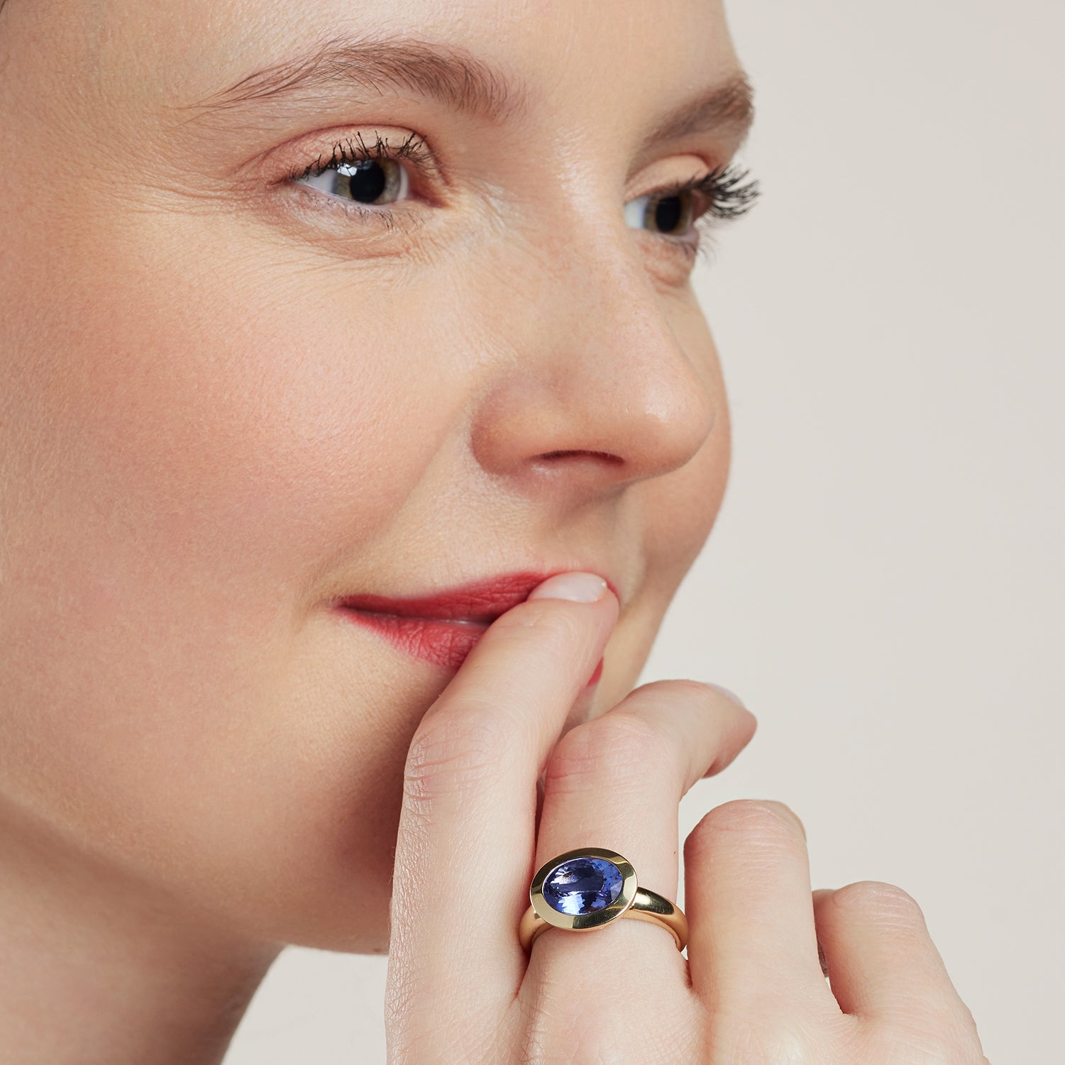 Eine Frau hält ihre Hand an den Mund; am Mittelfinger trägt sie einen Band-Ring in Gelbgold mit einem in Gelbgold quer gefassten, ovalen, blauen Stein;
