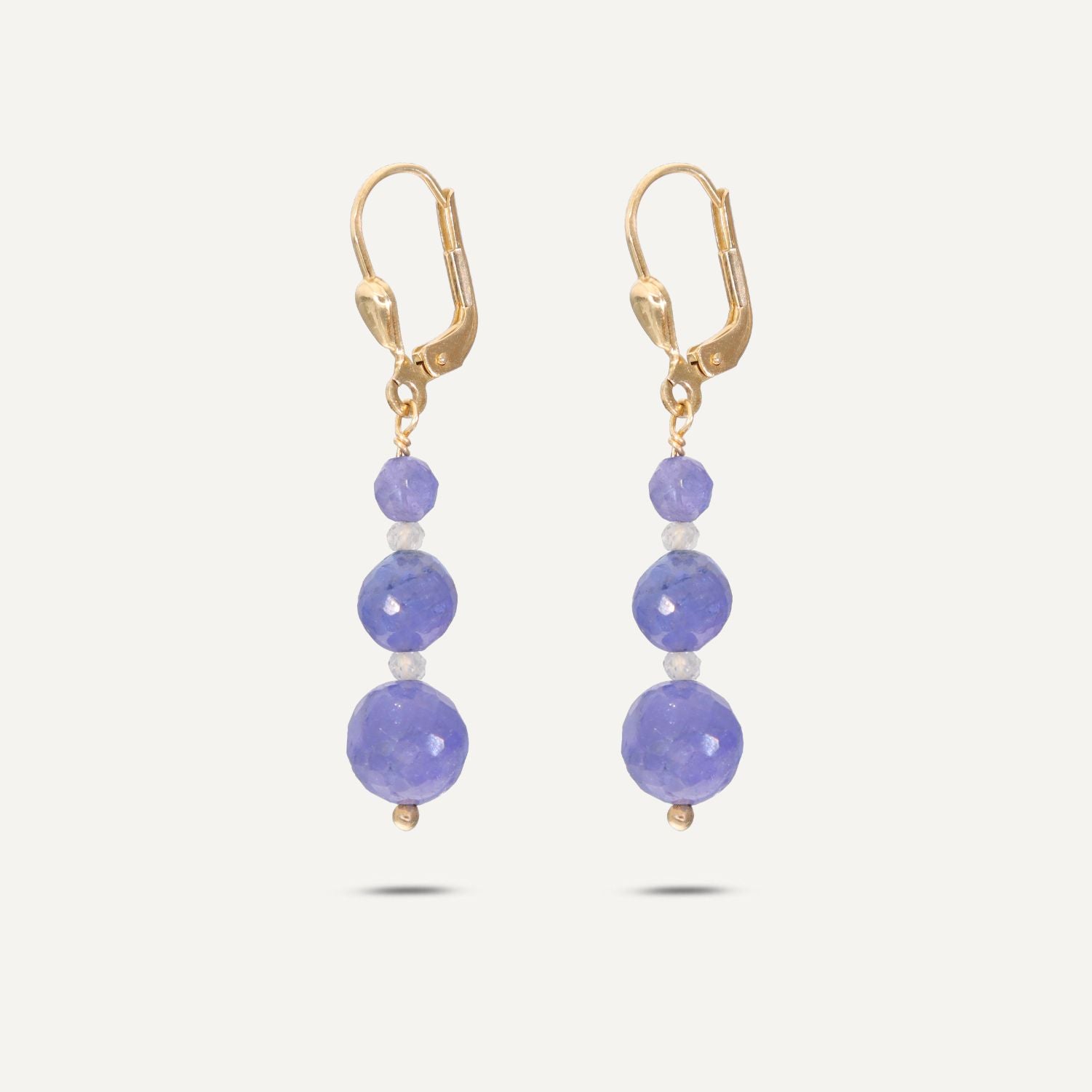 Ohrhänger in Gold mit drei runden, jeweils nach unten größer werdenden, blauen Steinen; zwischen den blauen Steinen ist jeweils ein kleiner, weißer, runder Stein; der Ohrhänger schießt unten mit einer goldenen, kleinen Kugel ab;