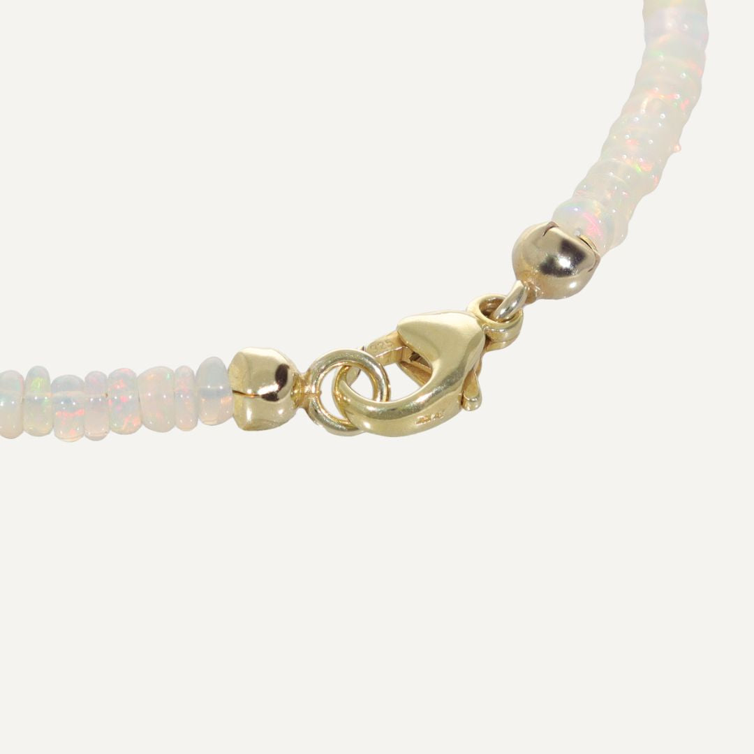 Ausschnitt des goldenen Karabinerverschlusses an einem Armband mit direkt aneinandergereihten hell schimmernden Kristallopalen;