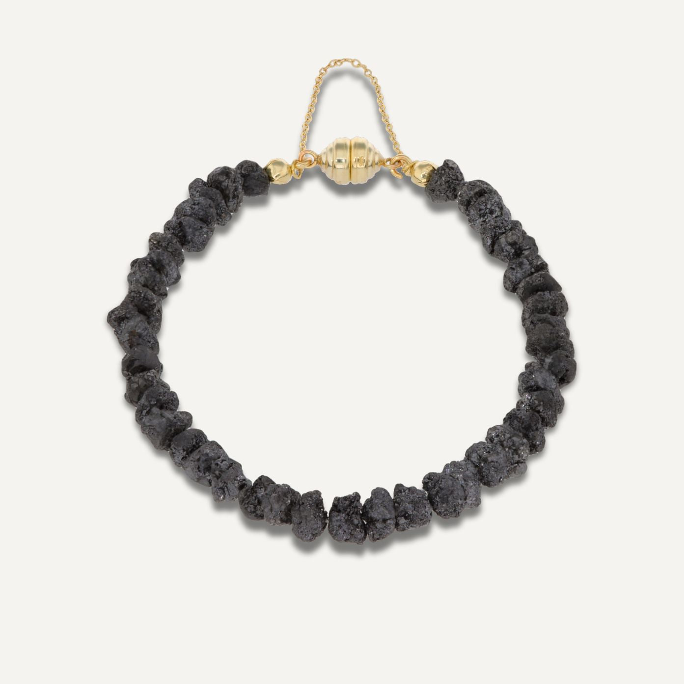 Armband aus direkt aneinander gereihten, unterschiedlich geformten, grau-schwarzen Rohdiamanten mit einer goldenen Magnetschließe mit Kette;