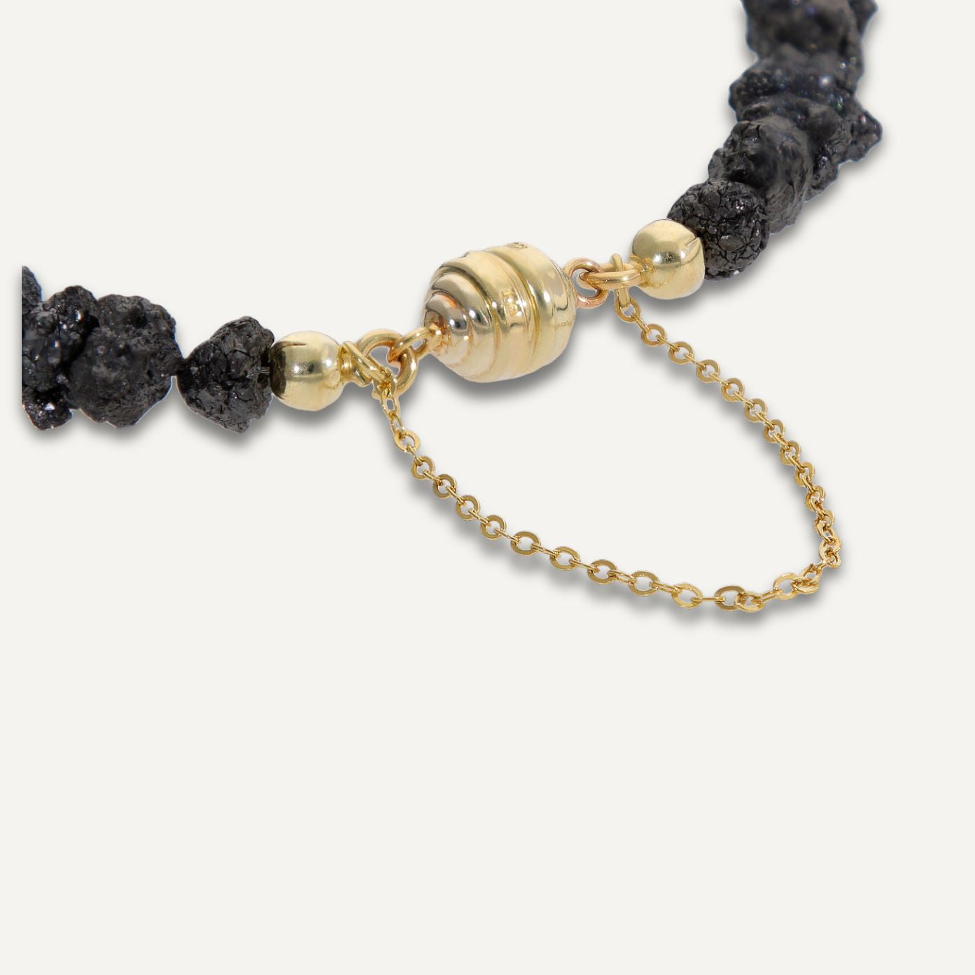 Ausschnitt der goldenen Magnetschließe mit Kette eines Armbands aus direkt aneinander gereihten, unterschiedlich geformten, grau-schwarzen Rohdiamanten;