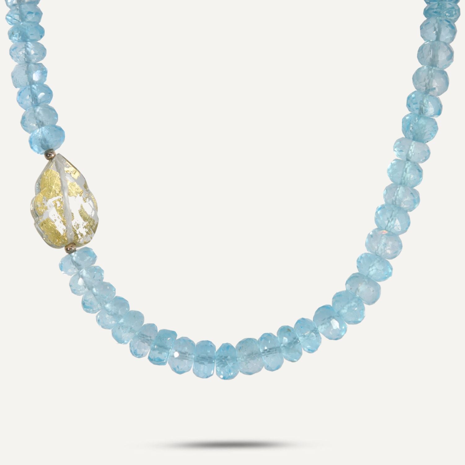 Collier aus direkt aneinander gereihten, hellblauen, durchsichtigen Steinen; links ist ein einzelner Kristall eingebunden;