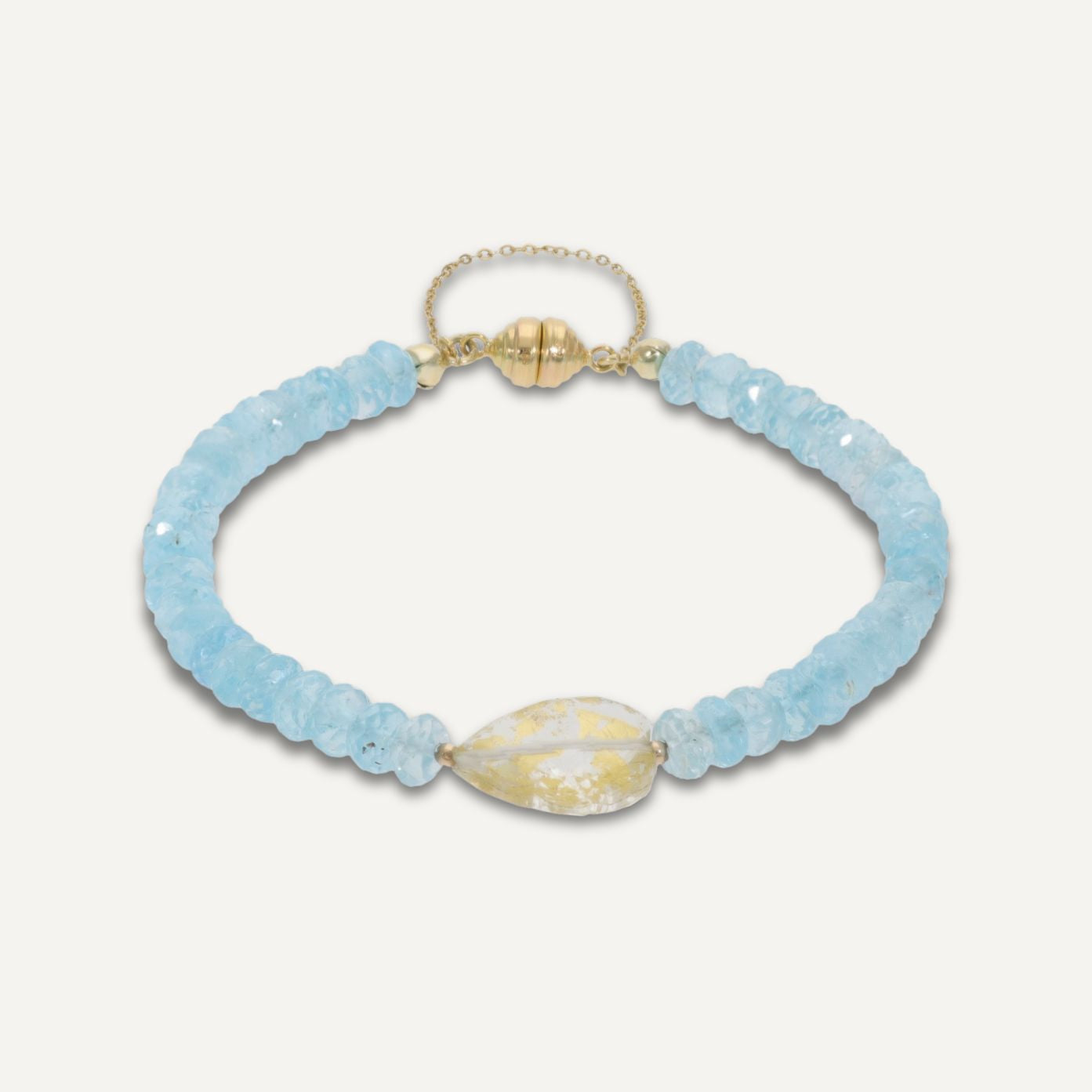 Armband aus direkt aneinander gereihten, hellblauen, durchsichtigen Steinen und einer goldenen Magnetschließe; mittig ist ein einzelner, größerer Kristall eingebunden;