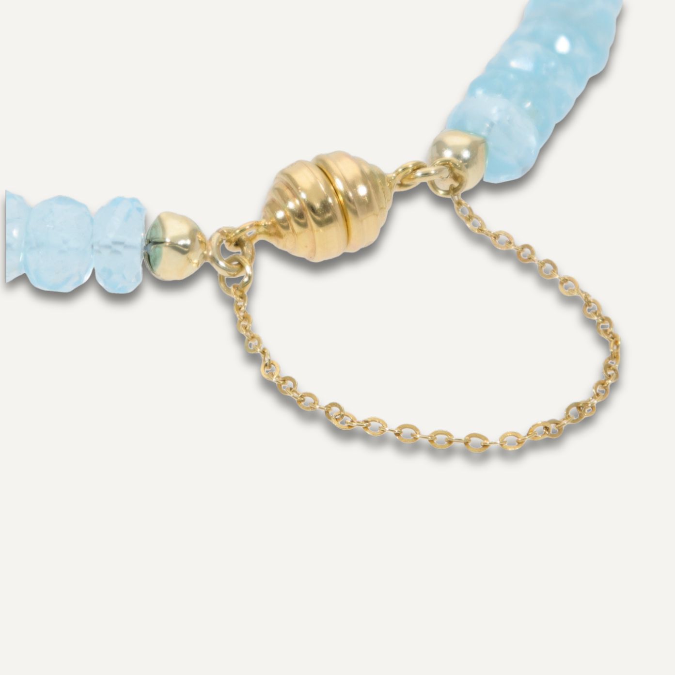 Ausschnitt der goldenen Magnetschließe eines Armbands aus direkt aneinander gereihten, hellblauen, durchsichtigen Steinen;