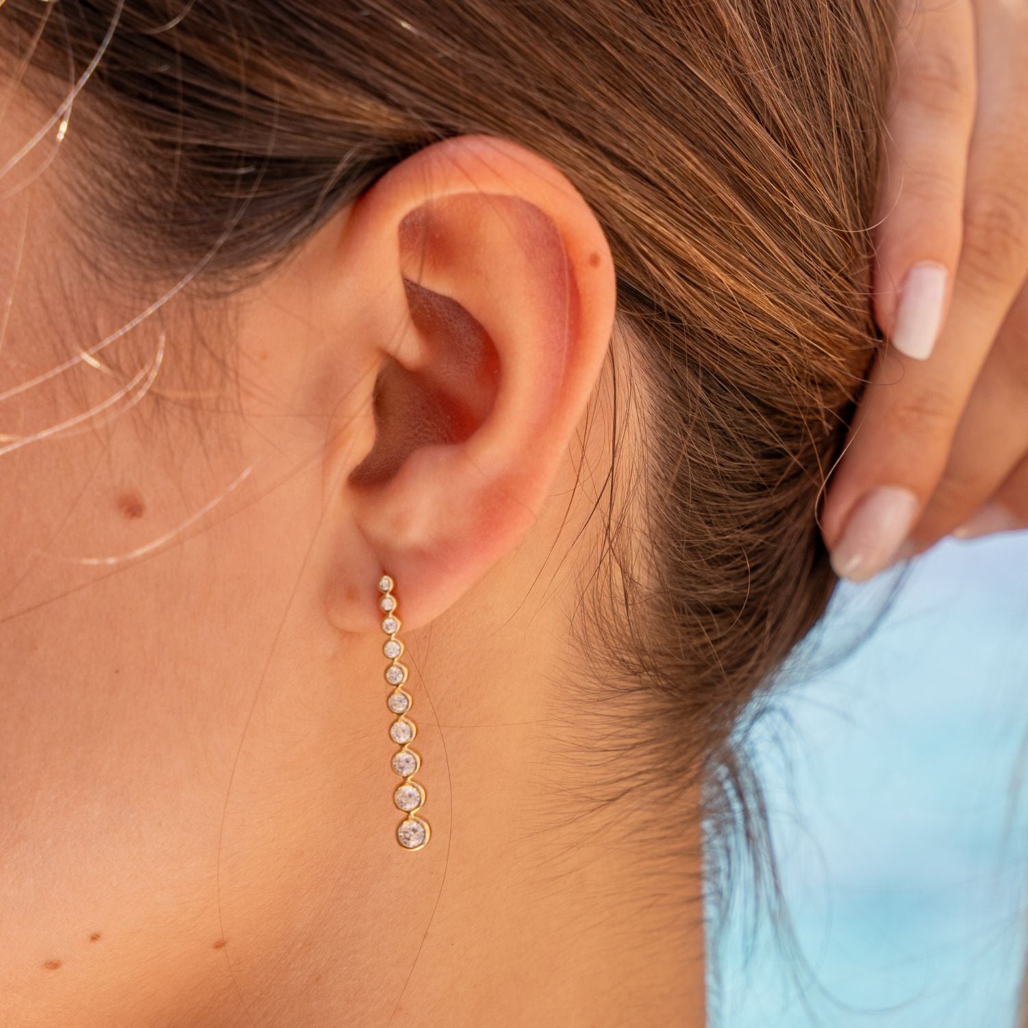 Ausschnitt des Profils einer Frau; sie hält ihre Haare nach hinten; am Ohr ein Ohrstecker in Gelbgold mit 10 in Gelbgold eingefassten, nach unten aneinander hängenden, größer werdenden, runden Zirkonen;