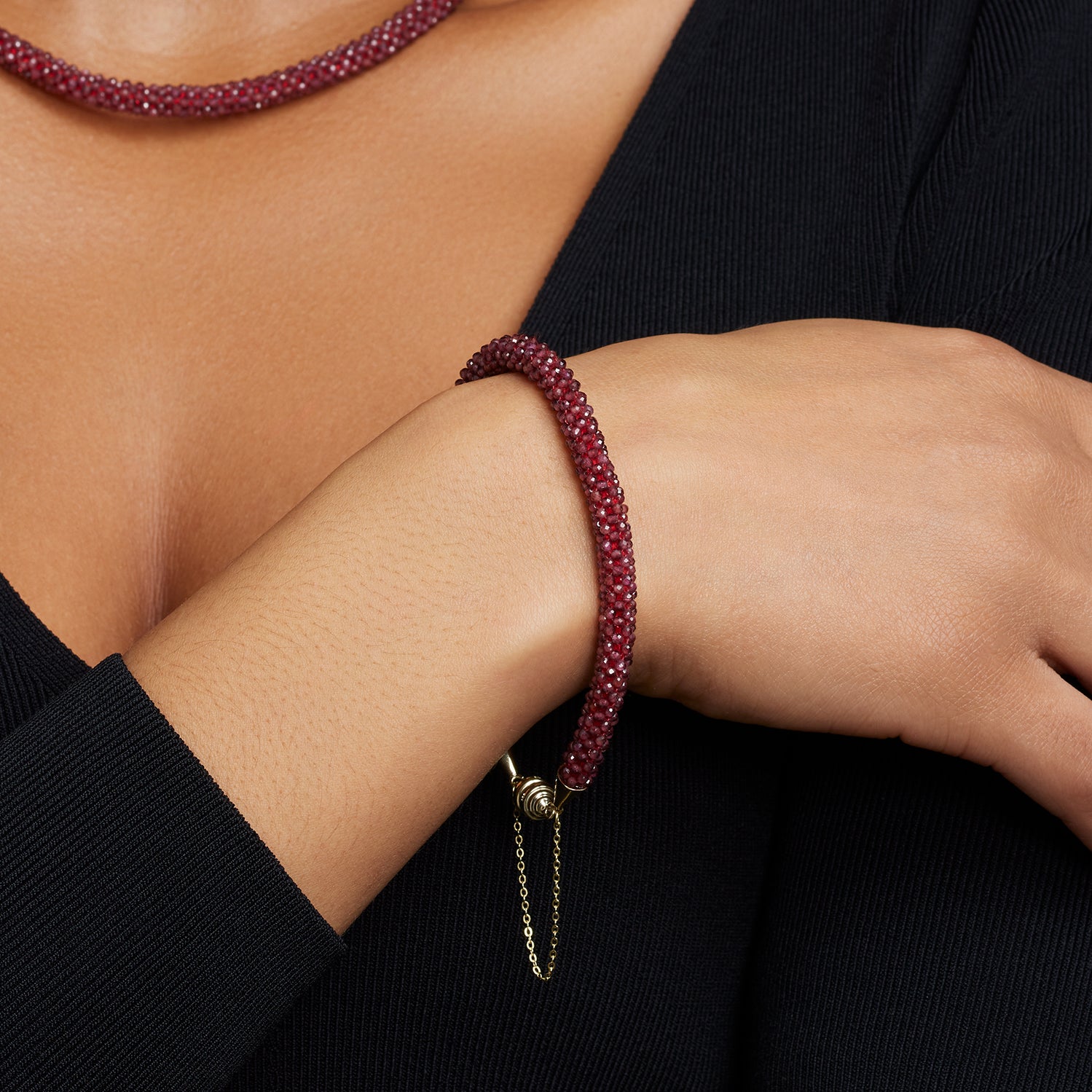 Ausschnitt des Halses und des Handgelenks einer Frau; sie trägt ein Collier und ein Armband aus vielen kleinen Rubin-Steinen in dunkelrot;