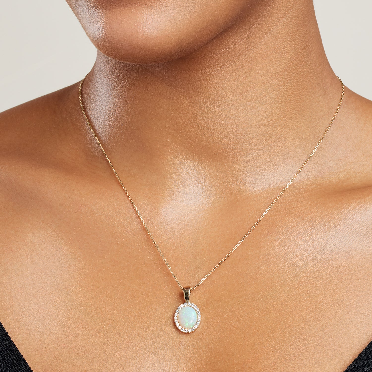 Ausschnitt des Halses einer Frau; sie trägt einen goldenen ovalen Clip-Anhänger mit einem mit Brillanten eingefassten bläulich schimmernden Kristallopal an einer goldenen Gliederkette;