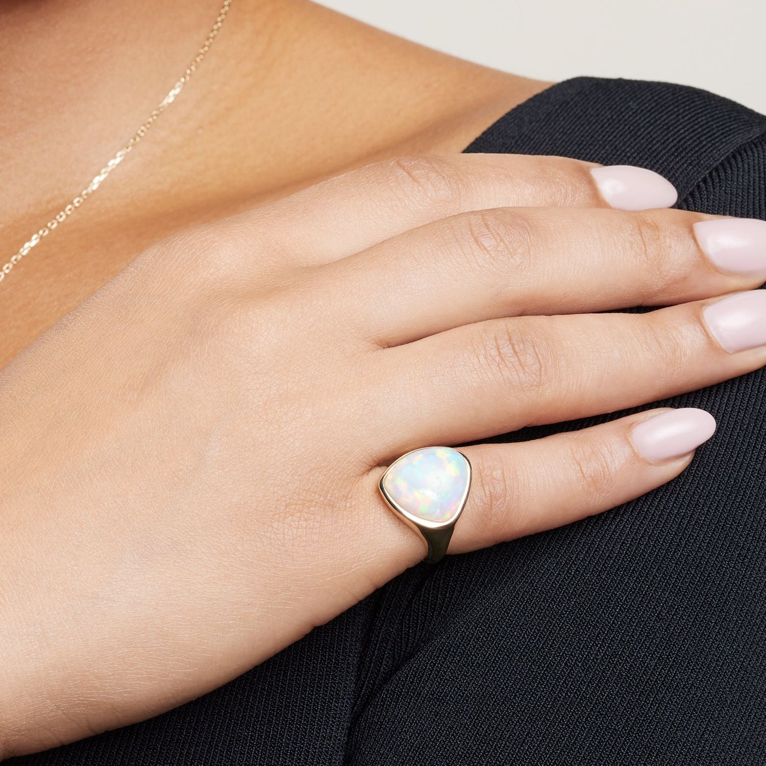 Ausschnitt der Hand einer Frau; sie trägt am kleinen Finger einen goldenen Band-Ring mit einem großen kreisbogenförmigen bläulich schimmernden Opal;