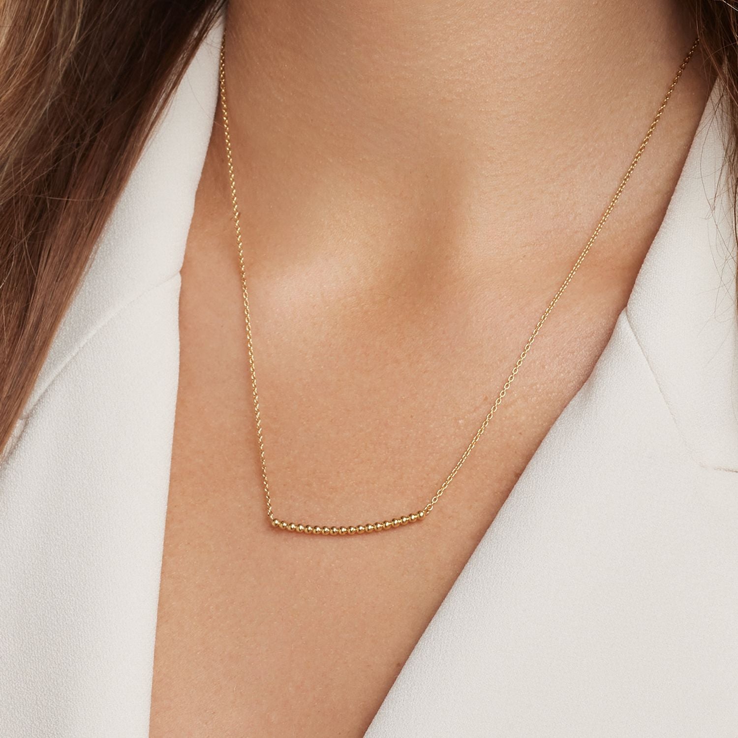 Halsausschnitt einer Frau; sie trägt eine feine goldene Gliederkette; in der Mitte 18 kleine goldene Kugeln;