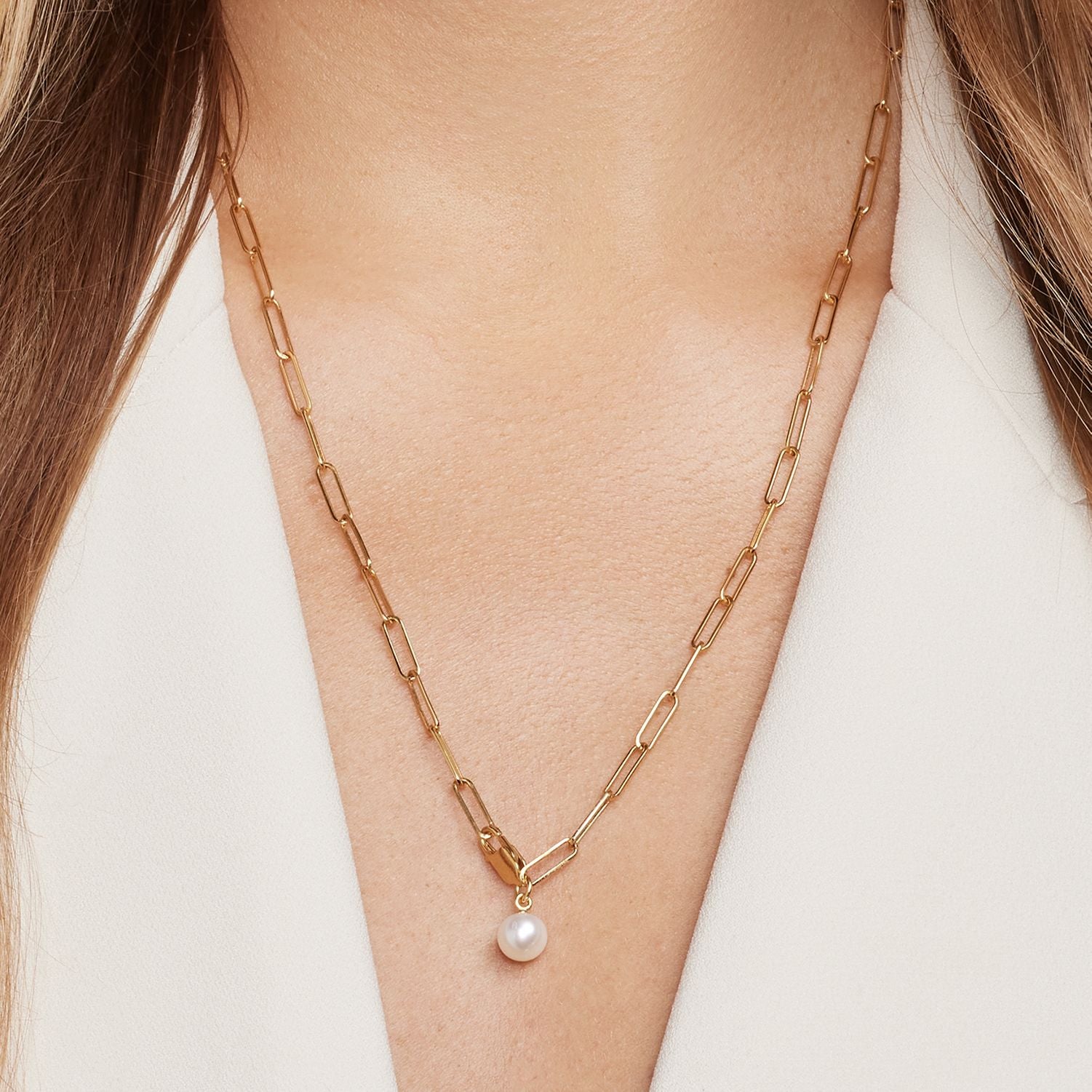 Halsausschnitt einer Frau; sie trägt eine goldene Gliederkette mit großen, feinen Gliedern und mit einer weißen Perle;