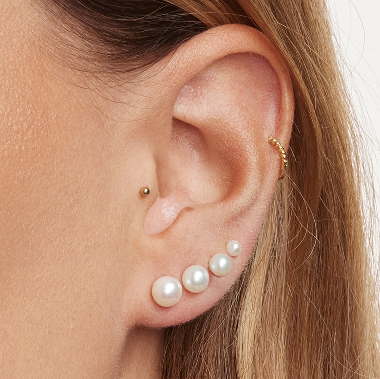 Ausschnitt eines Ohrs mit vier Perlen- Ohrsteckern in unterschiedlichen Größen, einem Earcuff mit goldenen Kugeln und einem kleinen, goldenen Kugel-Ohrstecker;