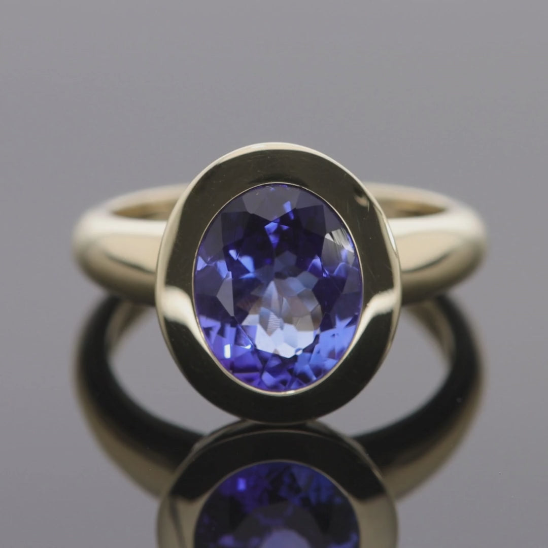 Das Video zeigt einen Band-Ring in Gelbgold mit einem in Gelbgold gefassten, ovalen, blauen Stein;