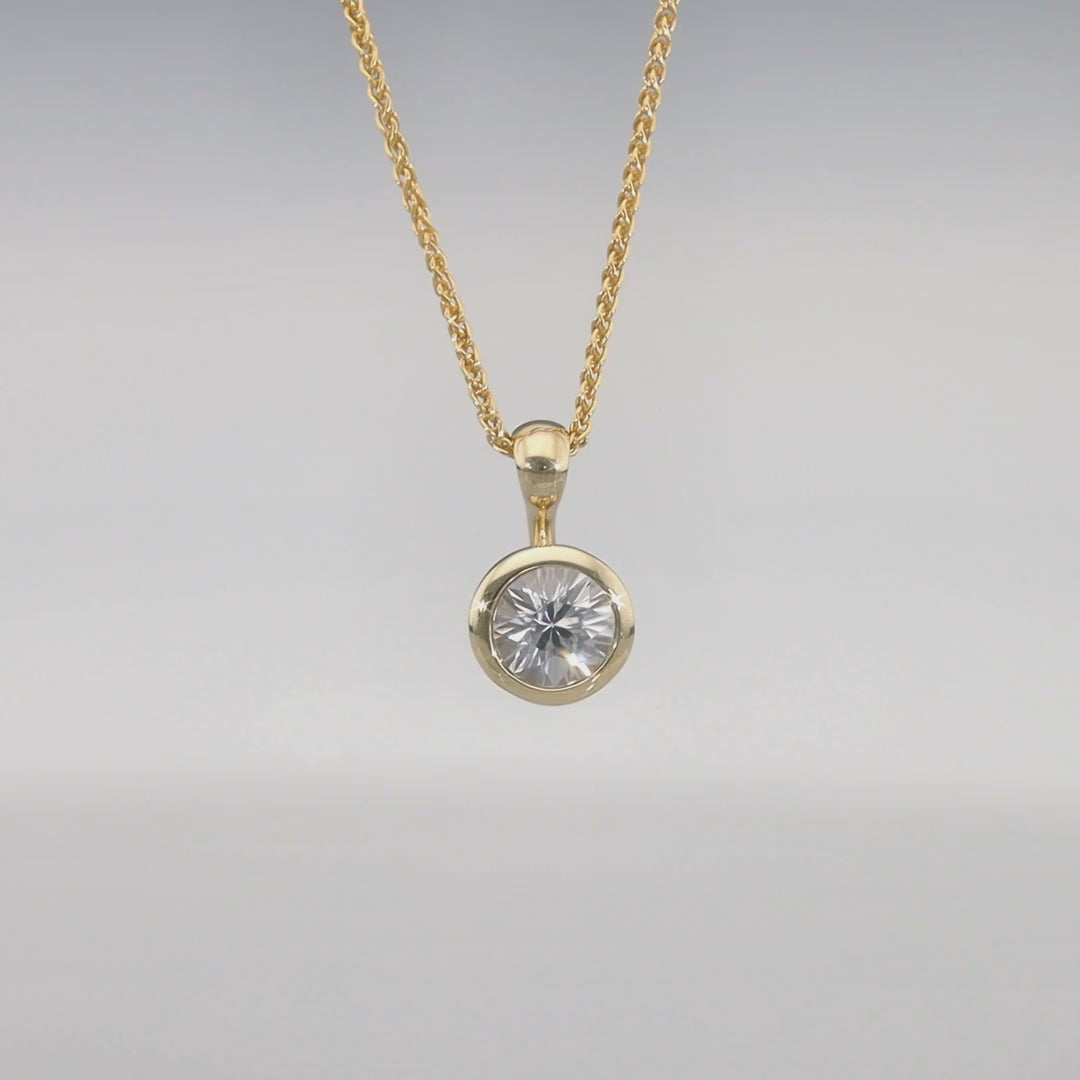 Das Video zeigt einen Clip-Anhänger aus Gelbgold mit einem in Gelbgold eingefassten, runden, weißen Zirkon an einer goldenen Kordelkette;