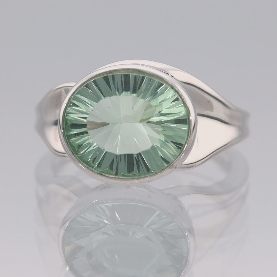 Das Video zeigt einen breiten Band-Ring in Silber mit einem eingefassten, ovalen, hellgrünen Stein;