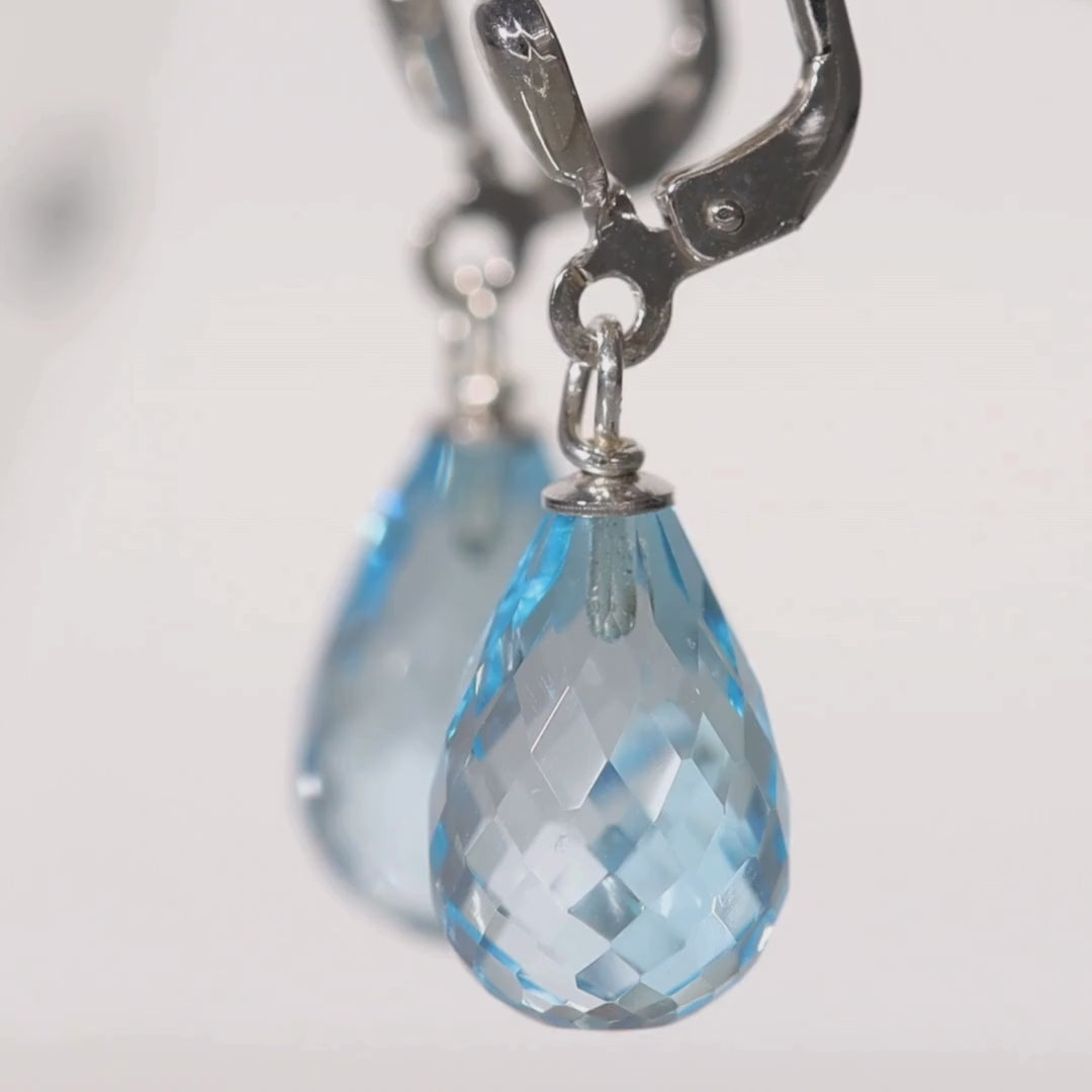 Das Video zeigt zwei Ohrhänger in Silber mit jeweils einem blauen, tropfenförmigen Stein;