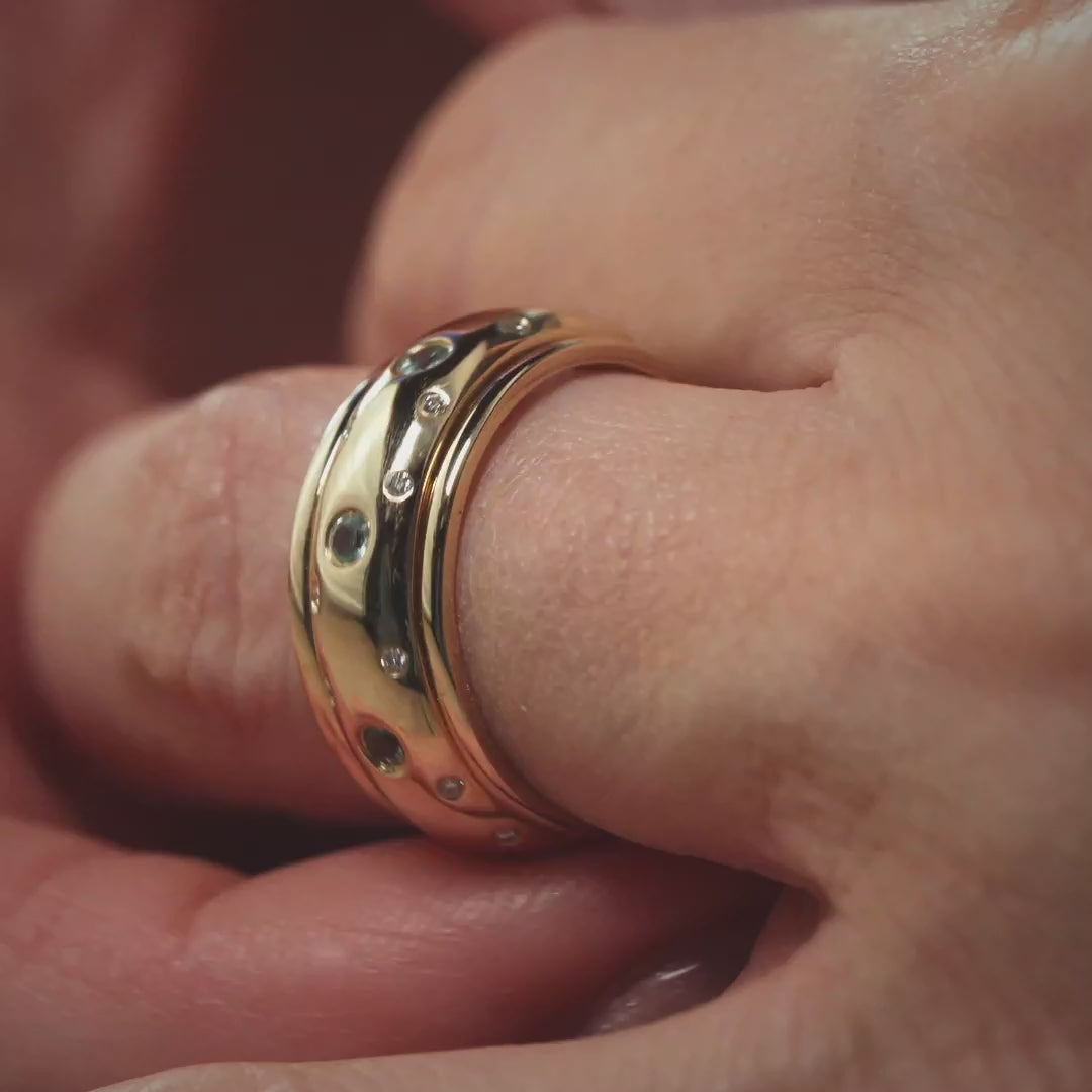 Das Video zeigt den Ausschnitt eines Fingers mit einem breiten Band-Ring in Gelbgold mit kleinen vereinzelten Brillanten außen und größeren weißen Steinen in der Mitte;