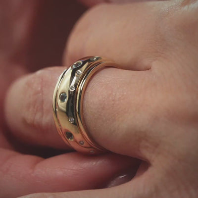 Das Video zeigt den Ausschnitt eines Fingers mit einem breiten Band-Ring in Gelbgold mit kleinen vereinzelten Brillanten außen und größeren weißen Steinen in der Mitte;